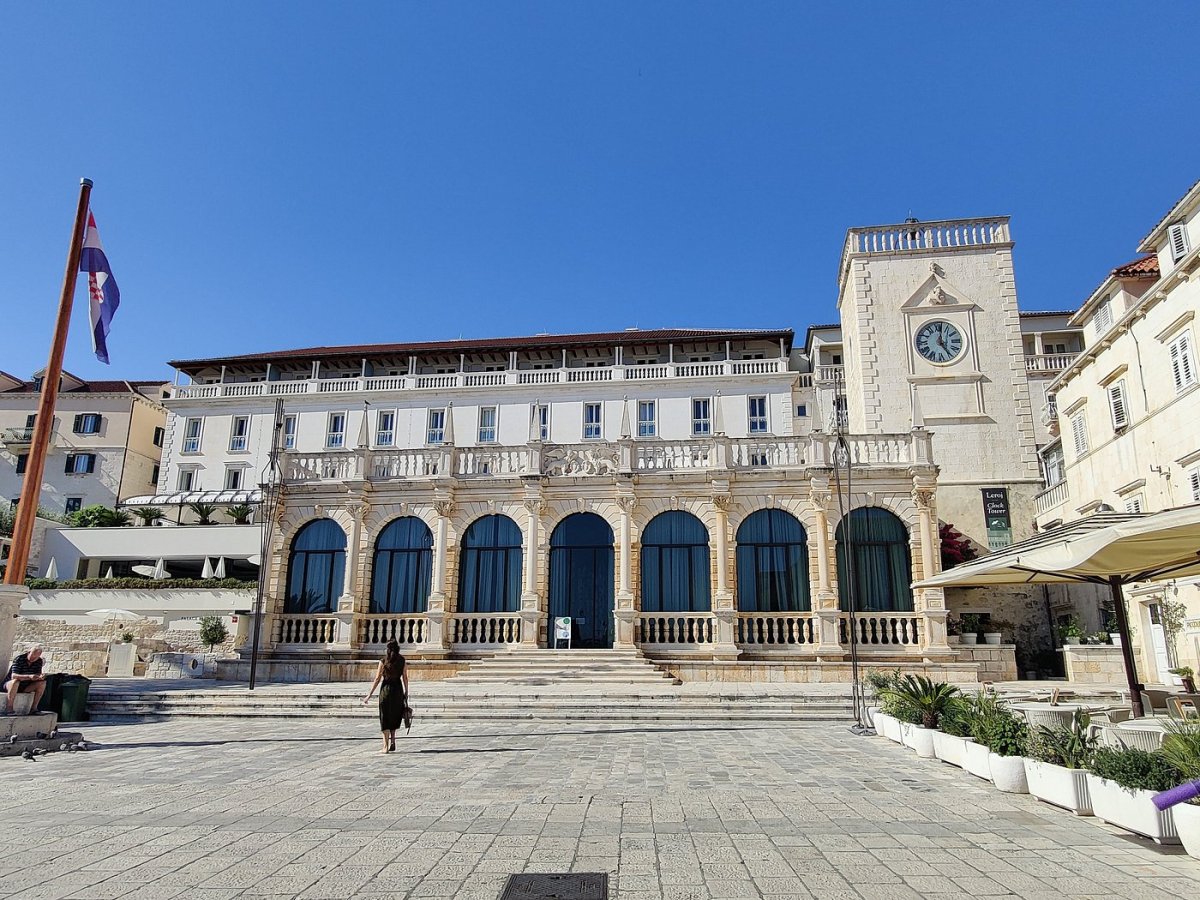 Historic stone arcade and clock tower on a sunlit Dalmatian town square