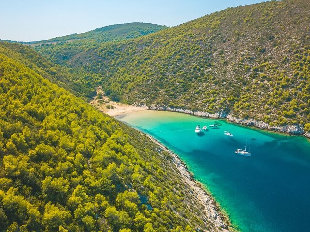 Aerial view of a secluded pine-lined cove with anchored yachts
