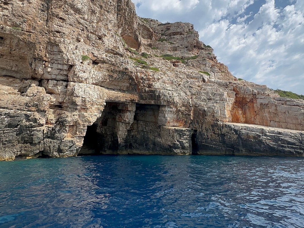 Steep limestone cliff with dark sea-cave openings above deep blue water