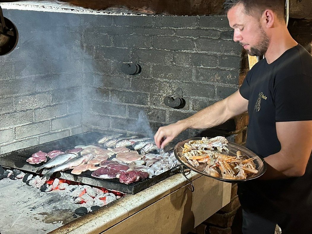 Chef grilling whole fish and seafood on a charcoal grill in Milna